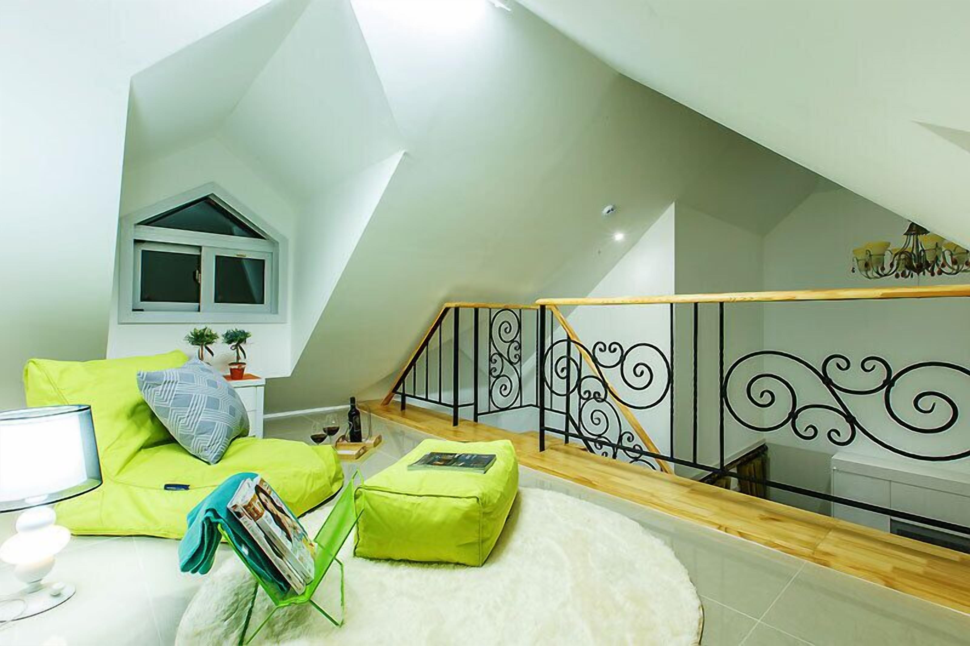 Un dormitorio tipo loft moderno con techo inclinado, una escalera de madera y un sofá blanco con cojines verdes.