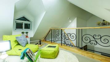Un dormitorio tipo loft moderno con techo inclinado, una escalera de madera y un sofá blanco con cojines verdes.