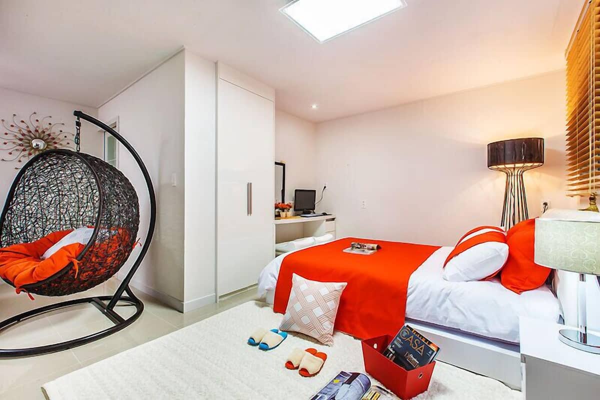 A modern bedroom with a bed, a hanging chair, a desk, and a lamp.