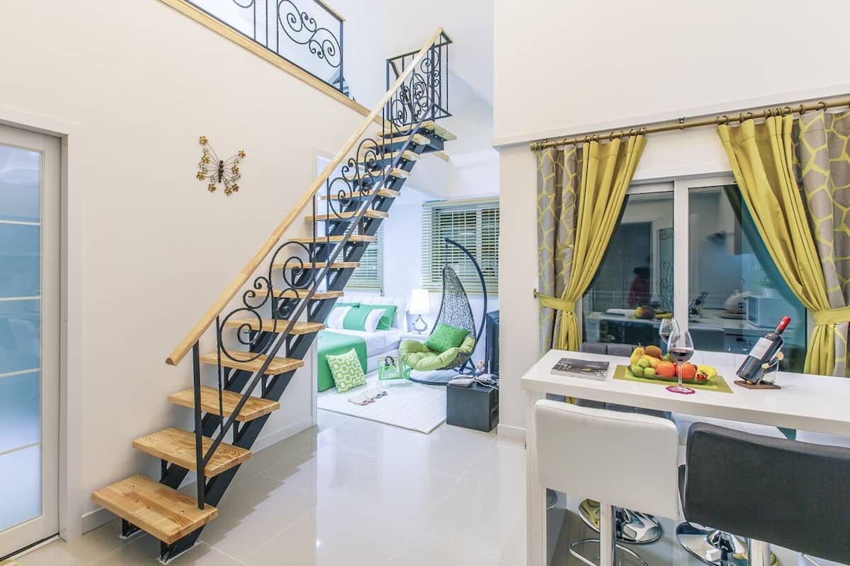 A modern interior with a wooden staircase, a dining area with a table set for two, and a living space with a sofa and green cushions.