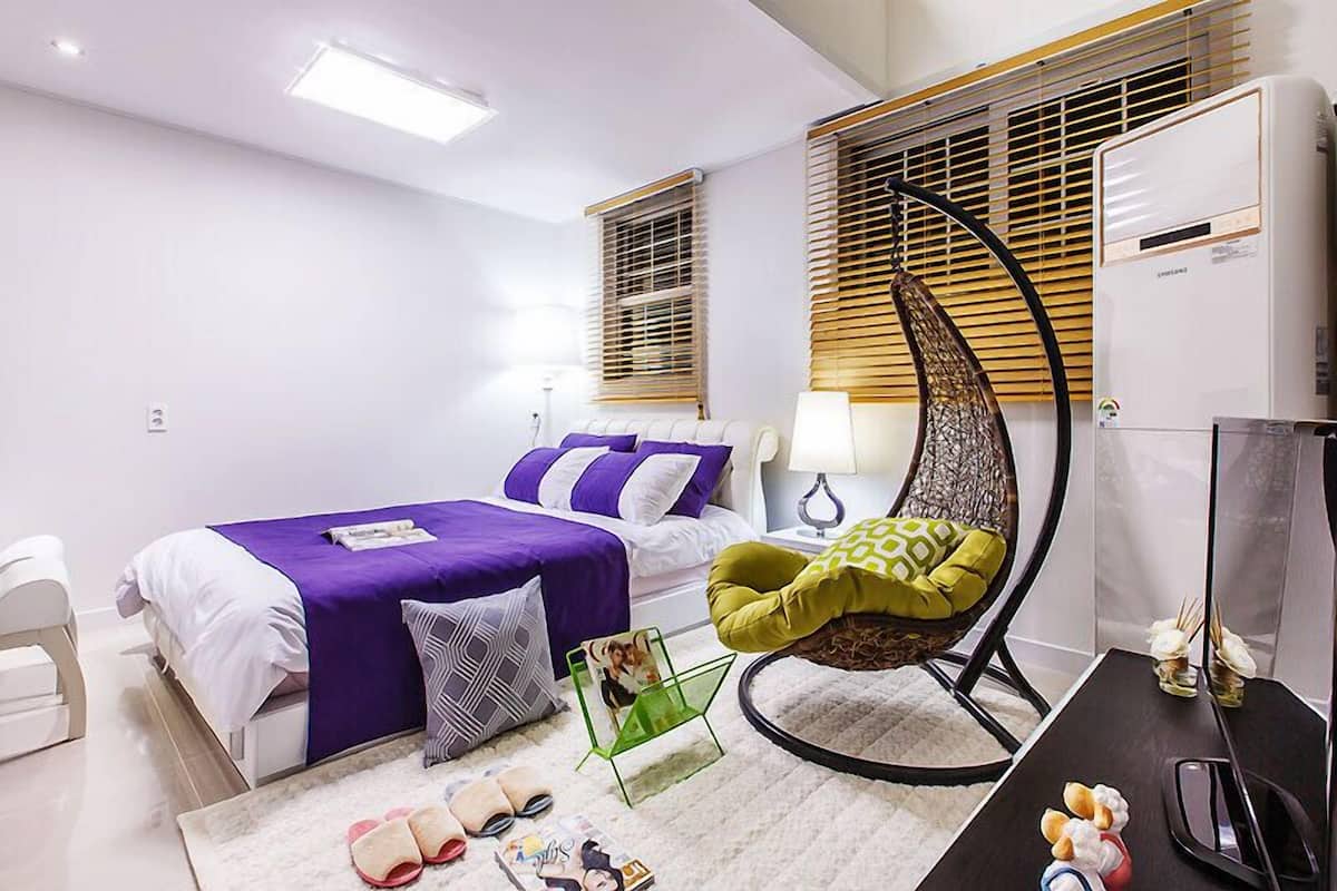 A modern bedroom with a bed, a chair, a desk, and a TV.