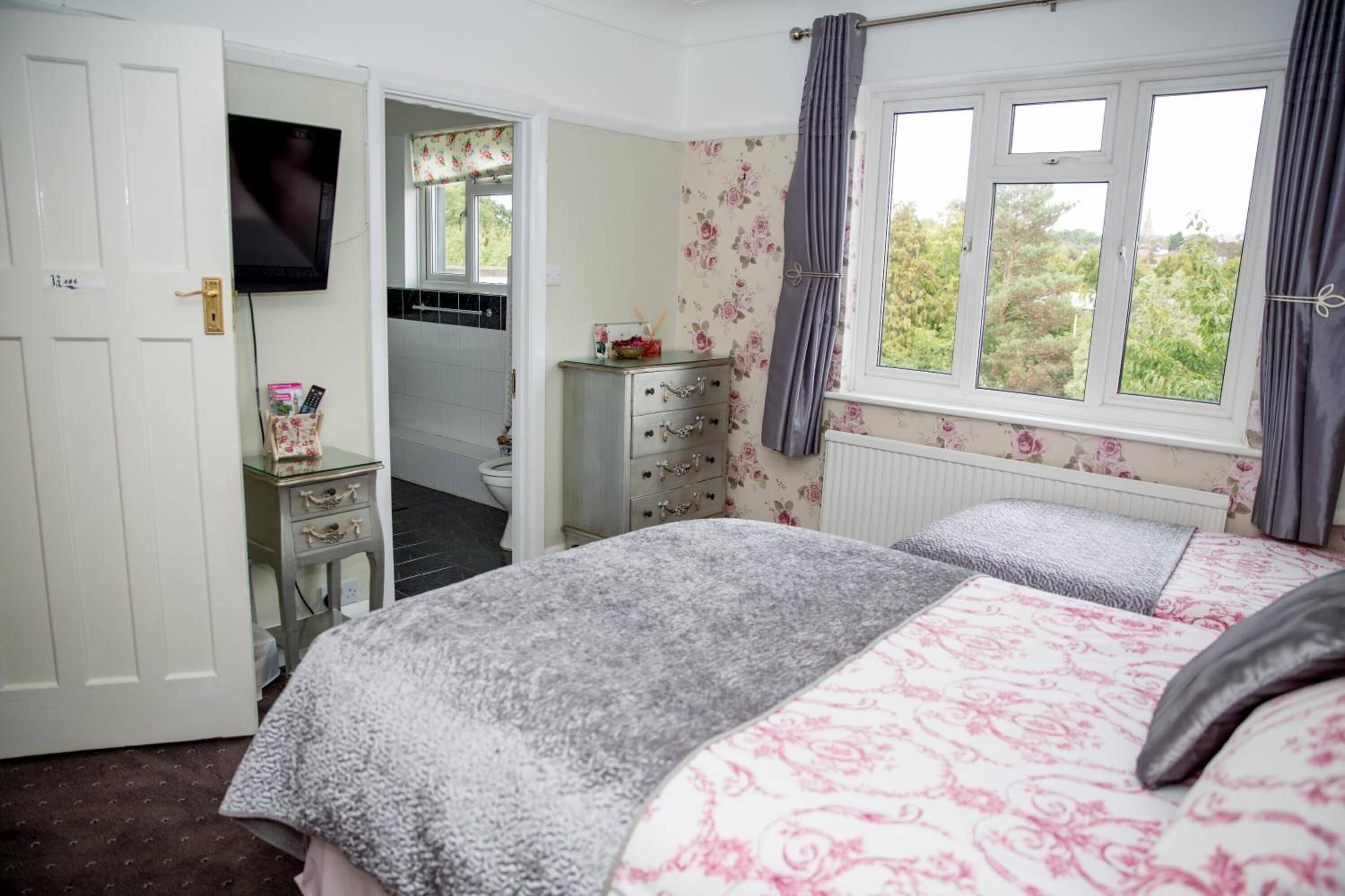 Un dormitorio con cama, cómoda, televisor y ventana con cortinas.