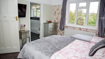 Un dormitorio con cama, cómoda, televisor y ventana con cortinas.