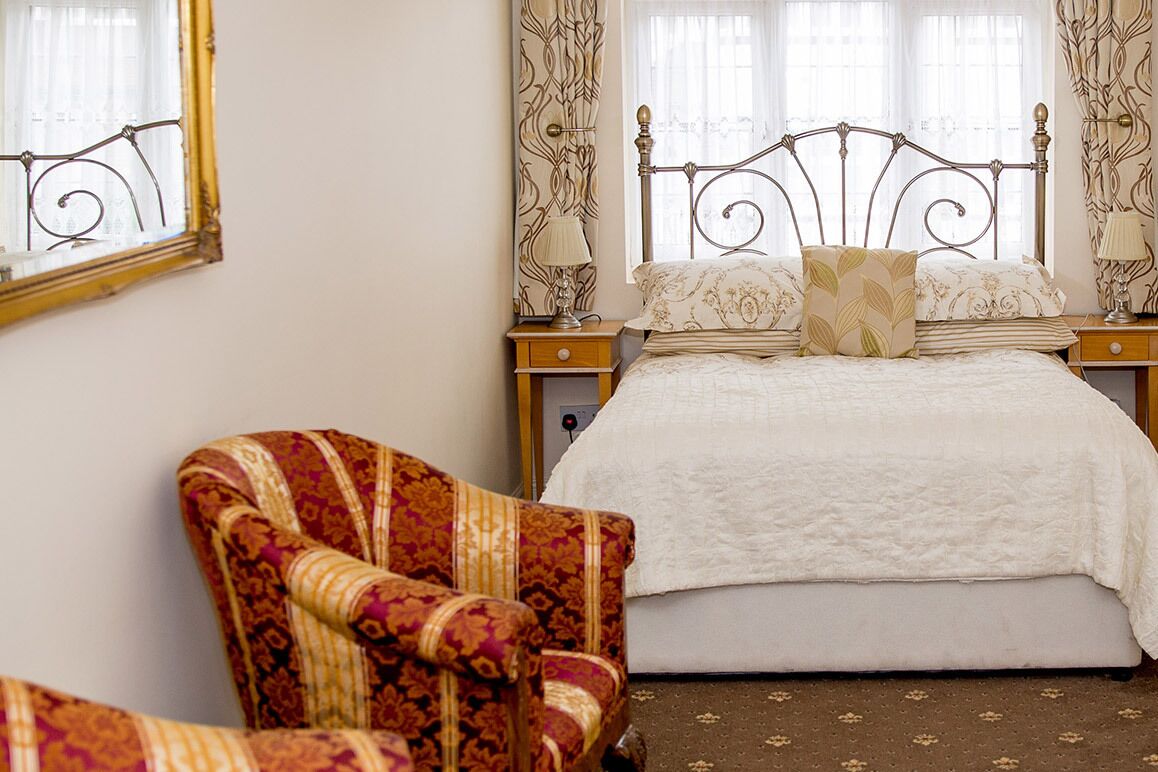 Un dormitorio con cama, dos mesitas de noche, una silla y cortinas.