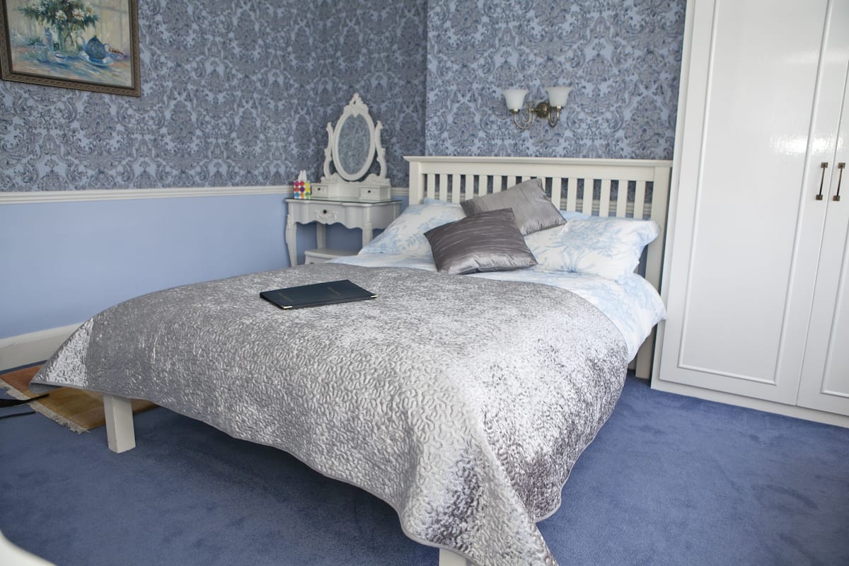 Une chambre à coucher comprenant un lit, une table de chevet, une commode et une lampe fixée au mur.