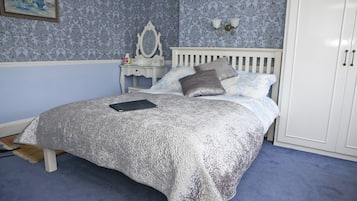 A bedroom with a bed, nightstand, dresser, and a wall-mounted lamp.