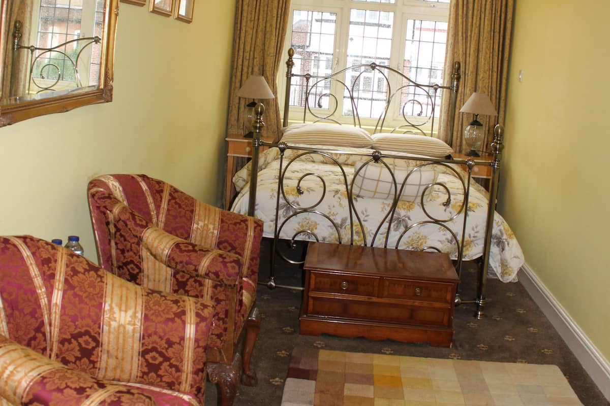 Une pièce comprenant un lit, deux fauteuils, une commode en bois, un tapis coloré et une fenêtre avec des rideaux.