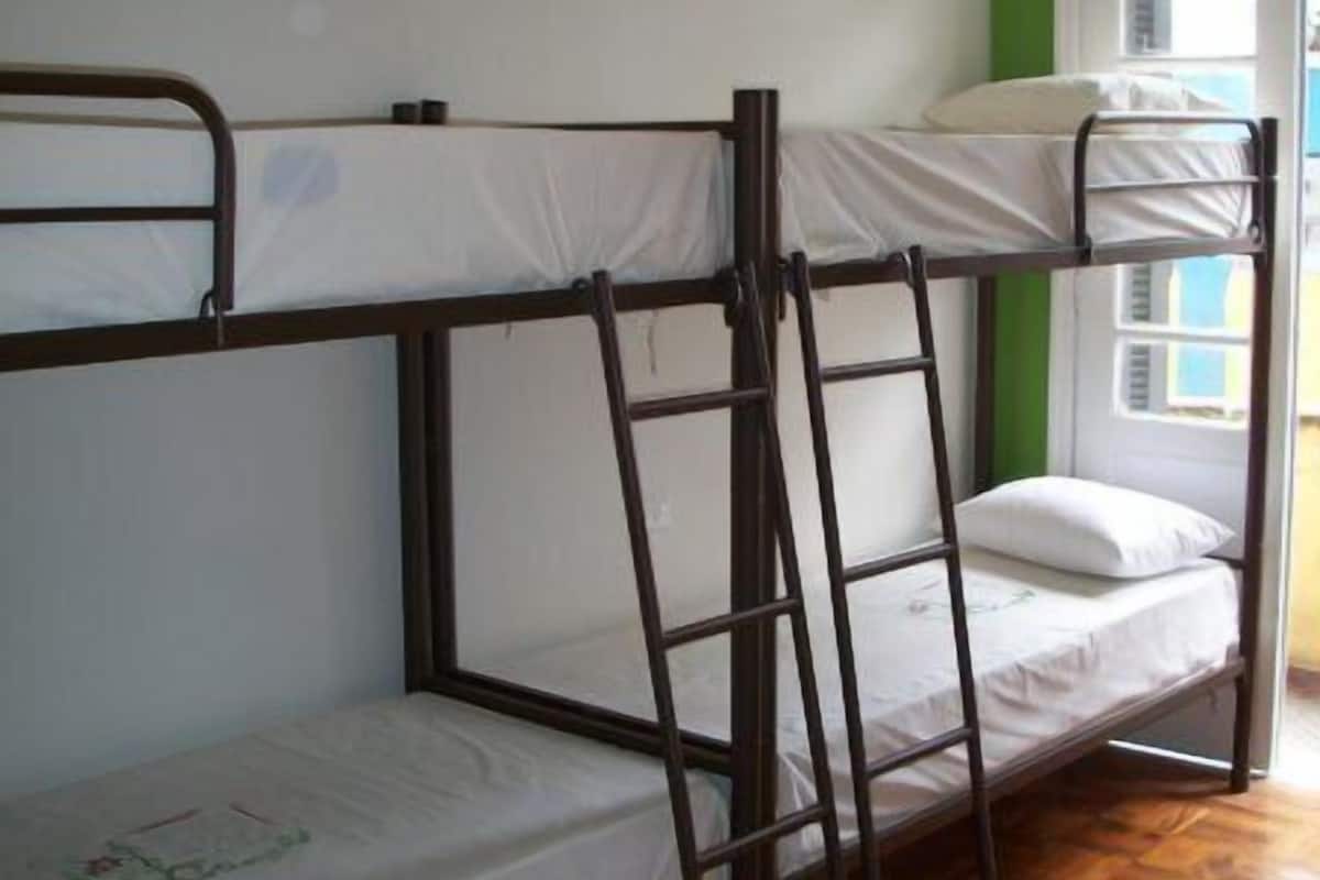 Una stanza dormitorio con letti a castello, pavimento in legno e una finestra con persiane.