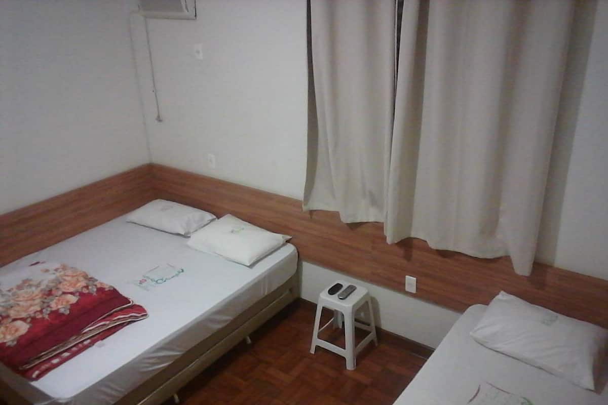 Una camera singola con un letto, uno sgabello e una finestra con tende.