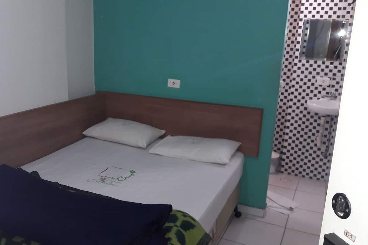 Piccola camera con un letto singolo, una testiera in legno, una coperta bianca e una trapunta blu.