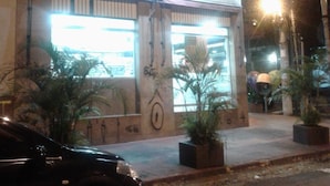 A building with a large illuminated sign, potted plants, and a parked car. - Hotel Pousada Clínicas Jardins Paulista (São Paulo)