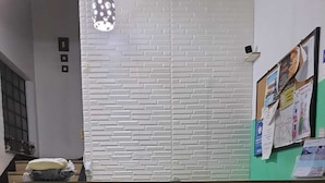 A reception area with a white brick-patterned counter, a small desk with a chair, a wall-mounted light fixture, and a bulletin board with various notices. - Hotel Pousada Clínicas Jardins Paulista (São Paulo)