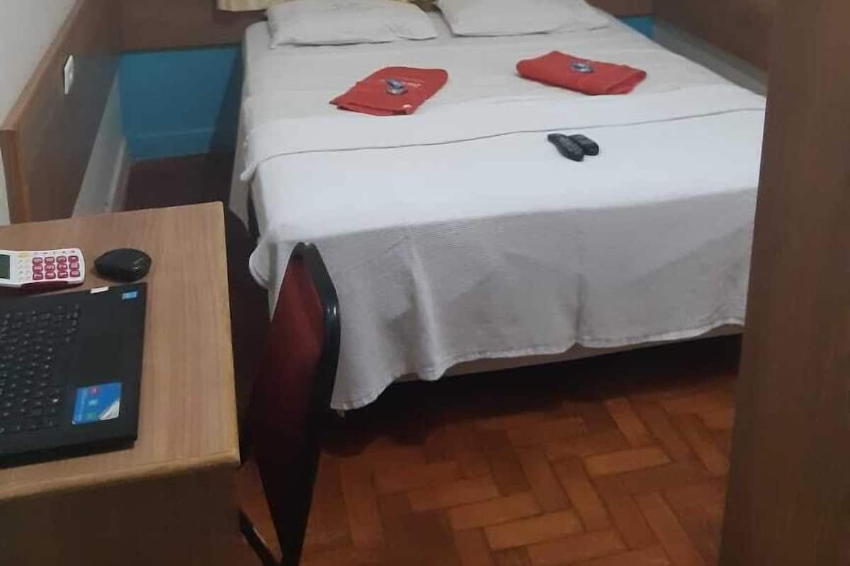 Una stanza piccola e ordinata, con un letto, una scrivania con un portatile e una tenda.