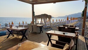 A beachside restaurant with wooden tables and chairs, umbrellas, and a view of the sea. - Bora Bora Butik Hotel (Alanya)