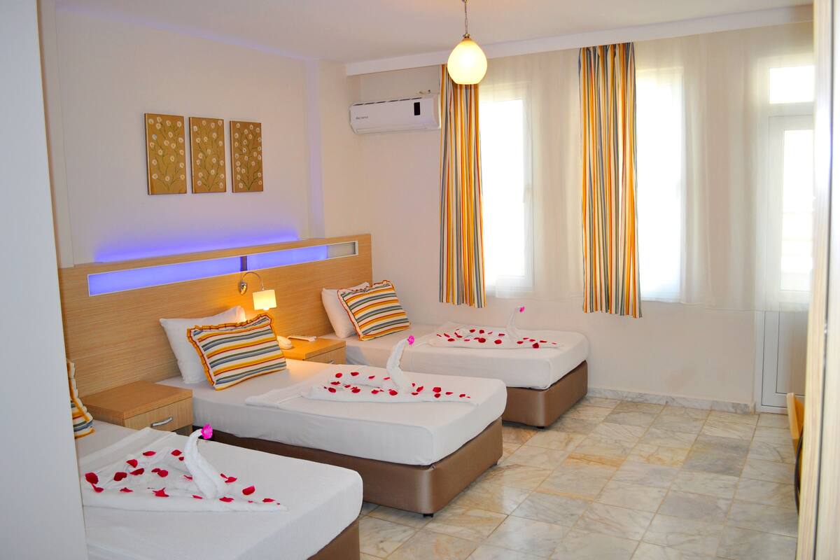 A hotel room with two beds, a nightstand, a lamp, a wall-mounted air conditioner, and a window with striped curtains.