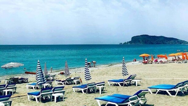 A beach with rows of sun loungers and umbrellas, a clear sky, and a calm sea. - Bora Bora Butik Hotel (Alanya)