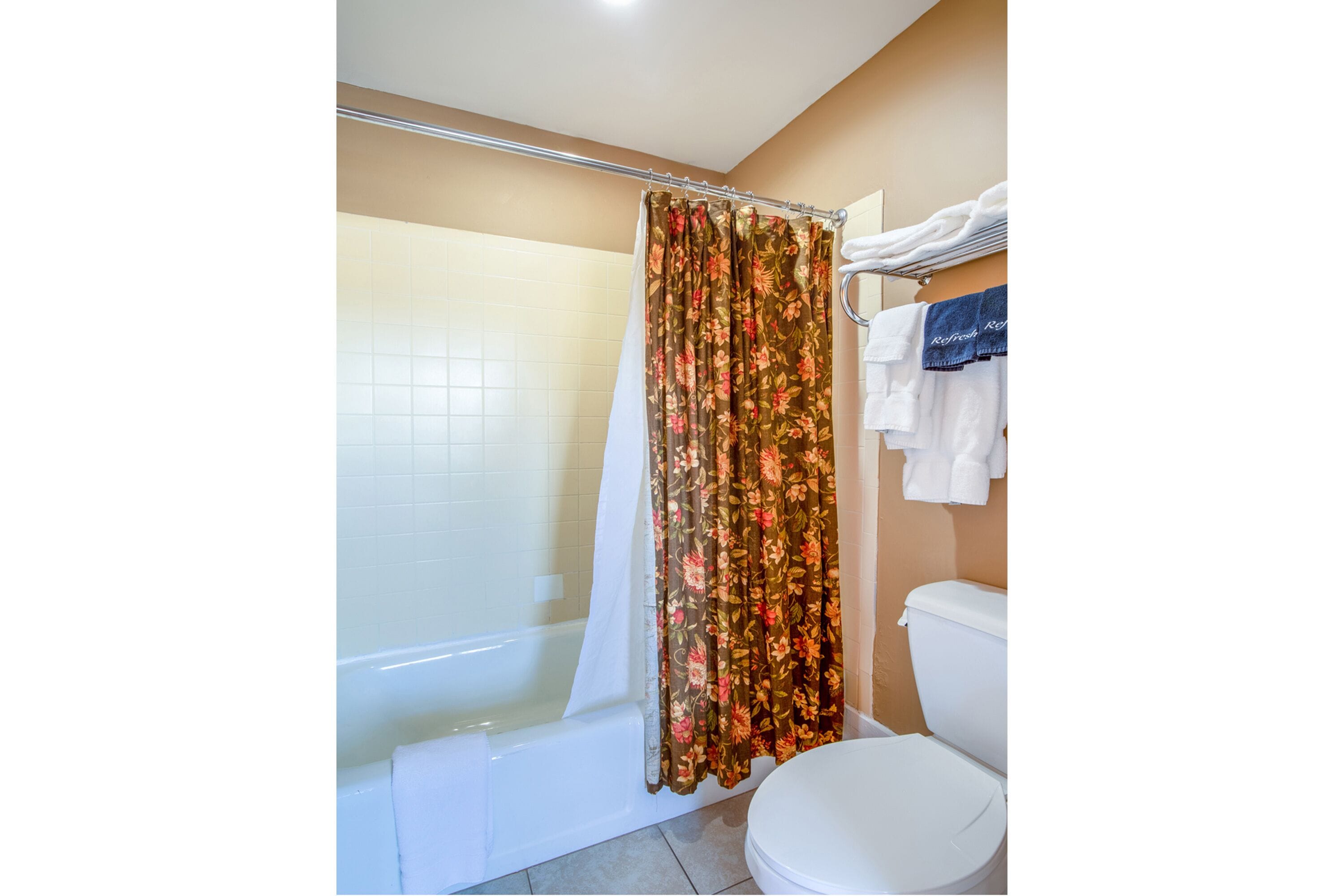 A bathroom with a shower, toilet, and a towel rack with towels.