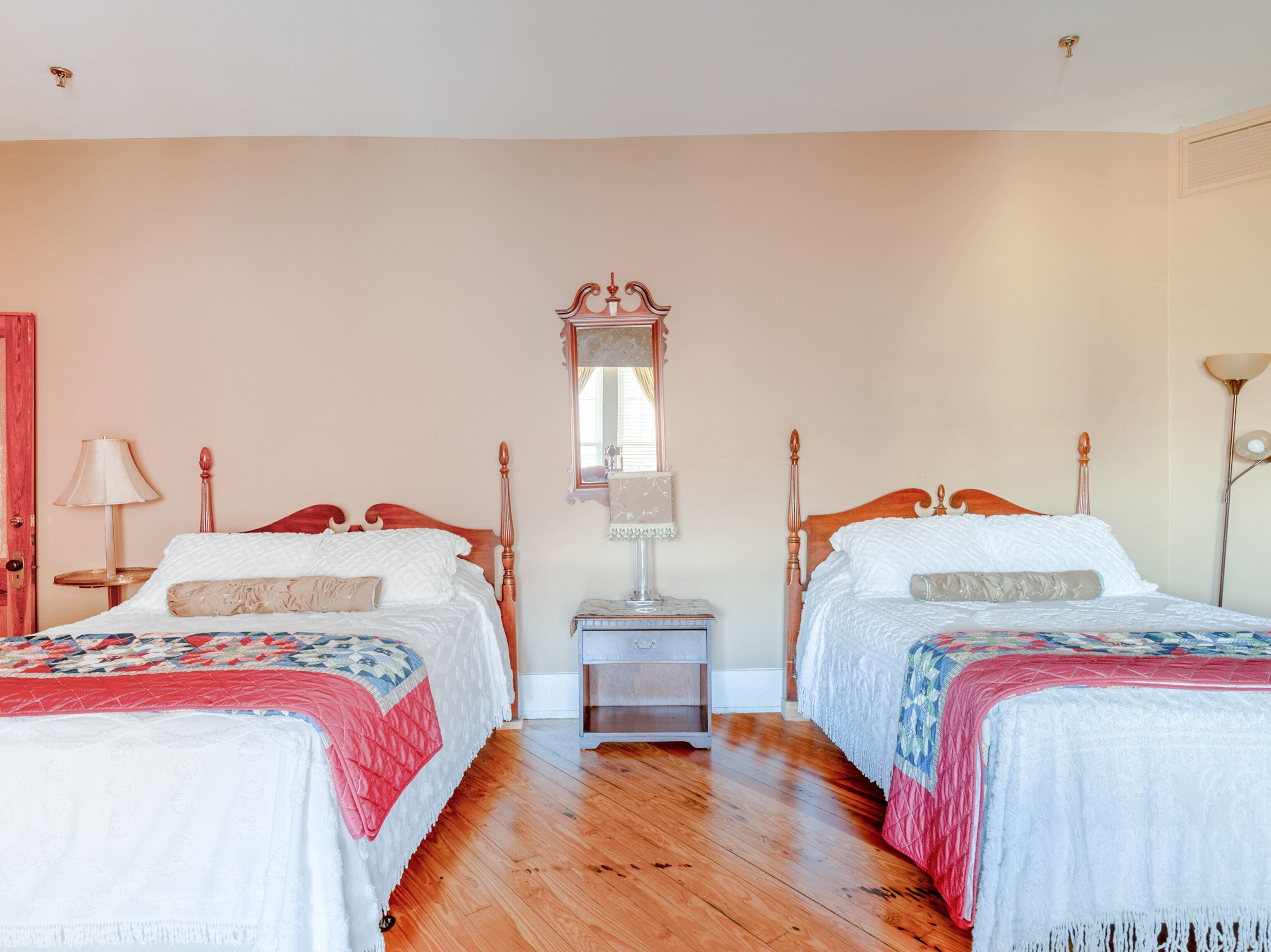 A bedroom with two wooden beds, a nightstand, a mirror, and a floor lamp.
