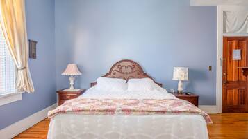 A bedroom with a wooden bed, two bedside tables with lamps, a window with curtains, and a door.