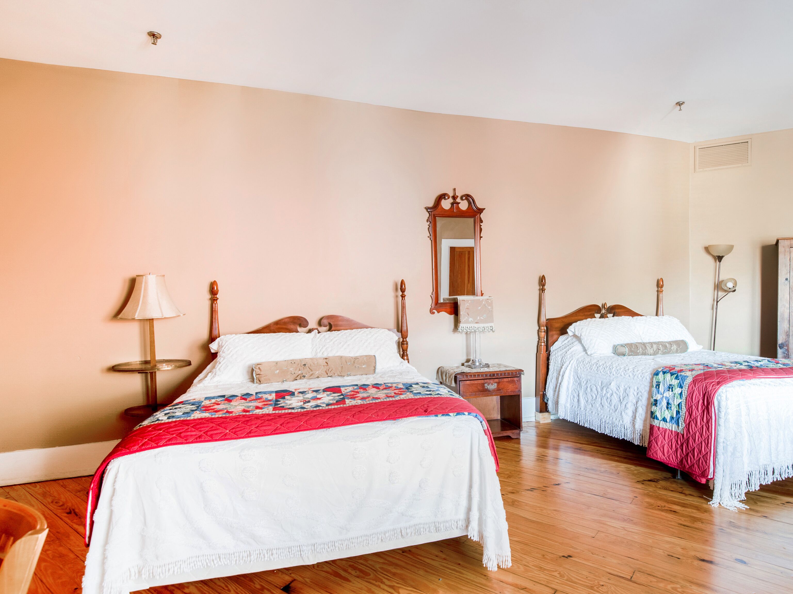 A hotel room with two wooden beds, a wooden nightstand, a mirror, and a lamp.