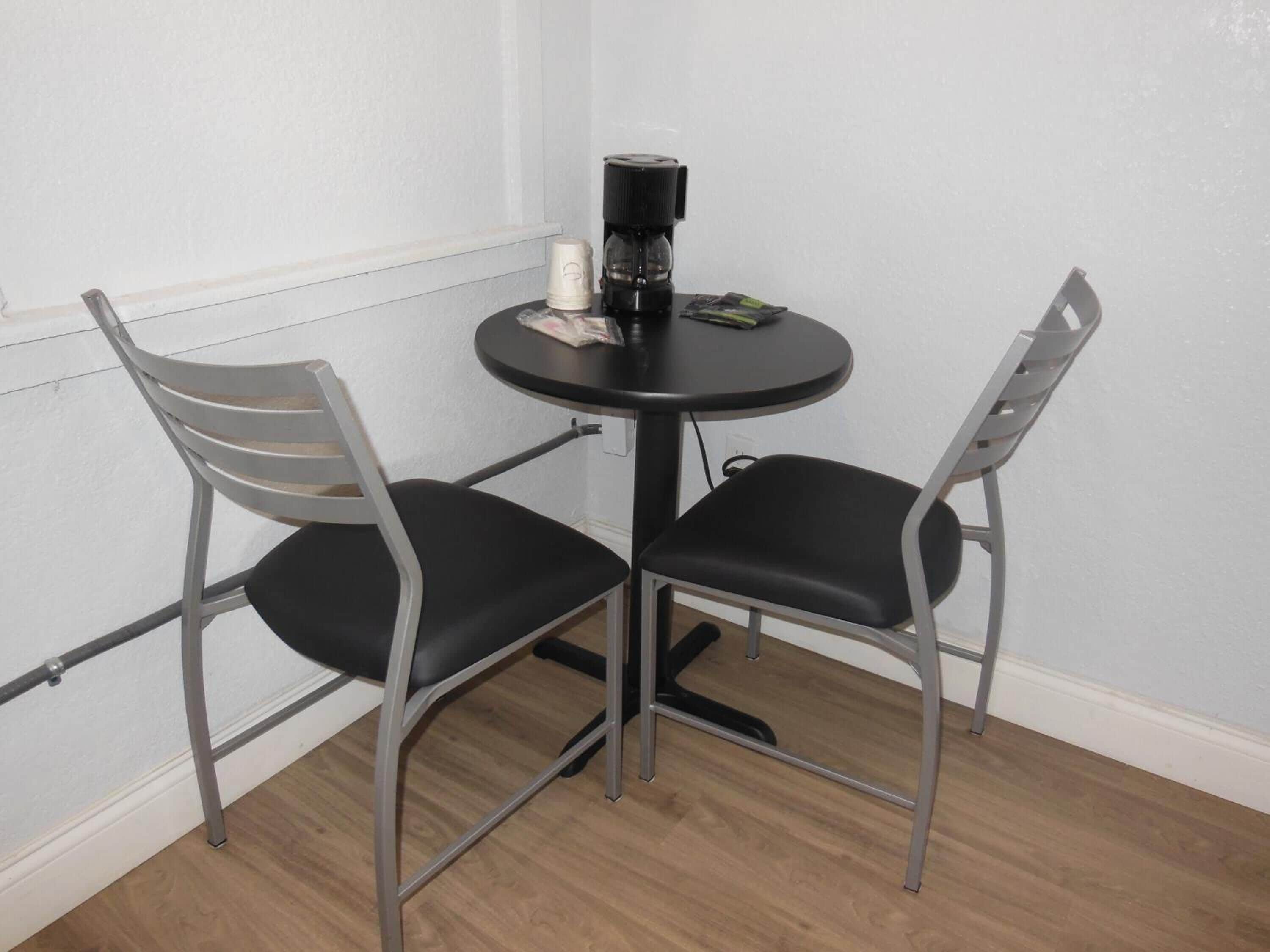 A small round table with two chairs, a coffee maker, and a remote control.