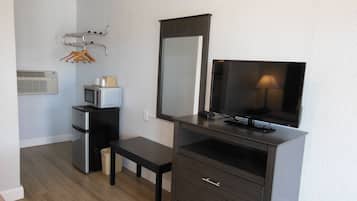 Habitación de hotel pequeña con kitchenette, un televisor de pantalla plana, un espejo y una pequeña banca.