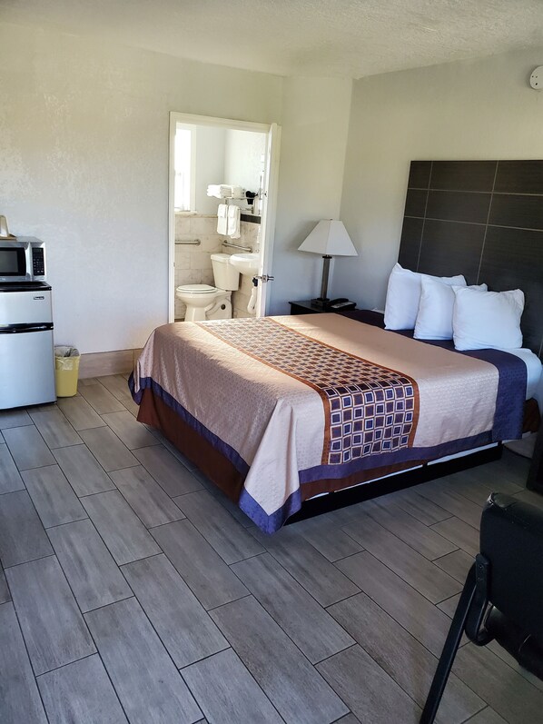 A hotel room with a bed, a nightstand, a lamp, a microwave, a sink, and a toilet.