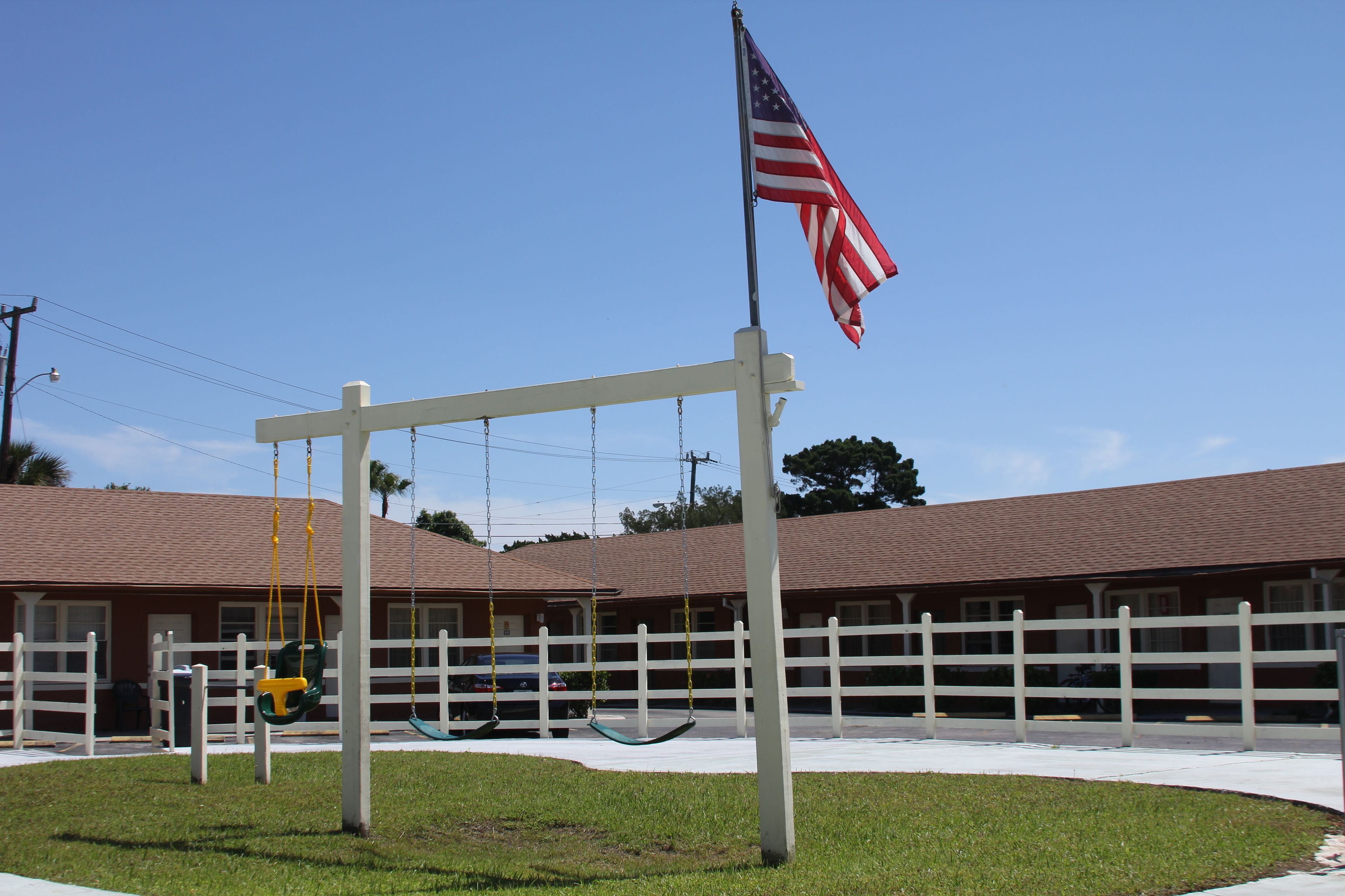 Un motel con valla blanca, un conjunto de columpios y una bandera estadounidense.