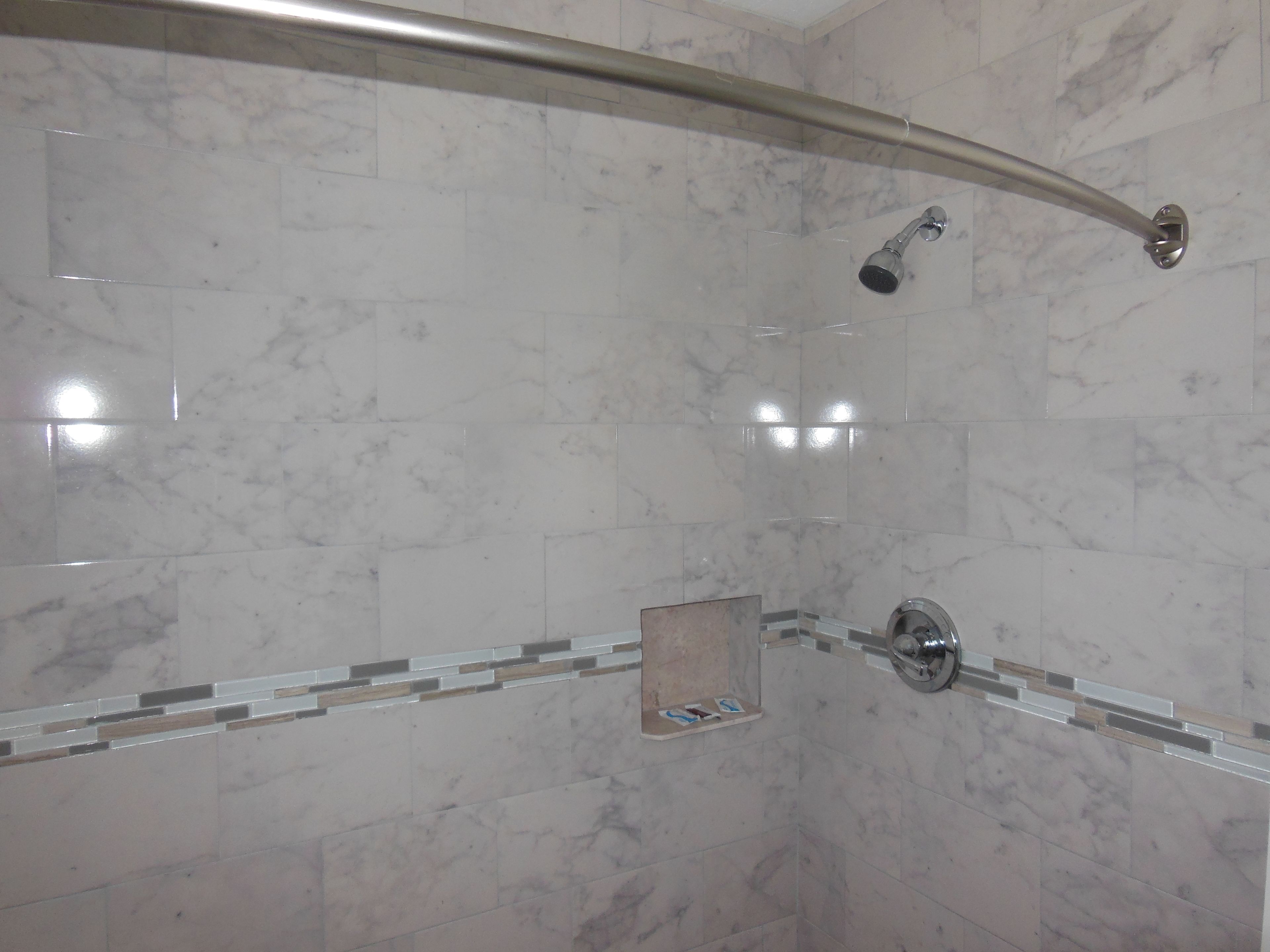 A modern bathroom with a curved showerhead, a glass shelf, and marble tiles.
