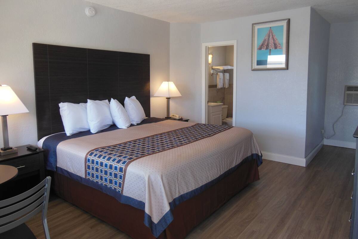 Habitación de hotel con una cama grande, dos lámparas de noche, una silla, un escritorio y un cuadro en la pared.