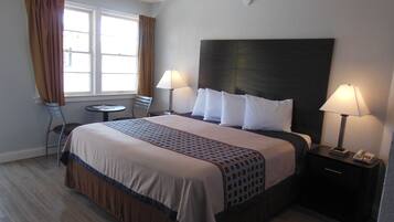 Una habitación de hotel con una cama grande, dos lámparas de noche, una mesita pequeña y una silla.
