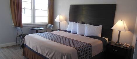 A hotel room with a large bed, two bedside lamps, a small table, and a chair.