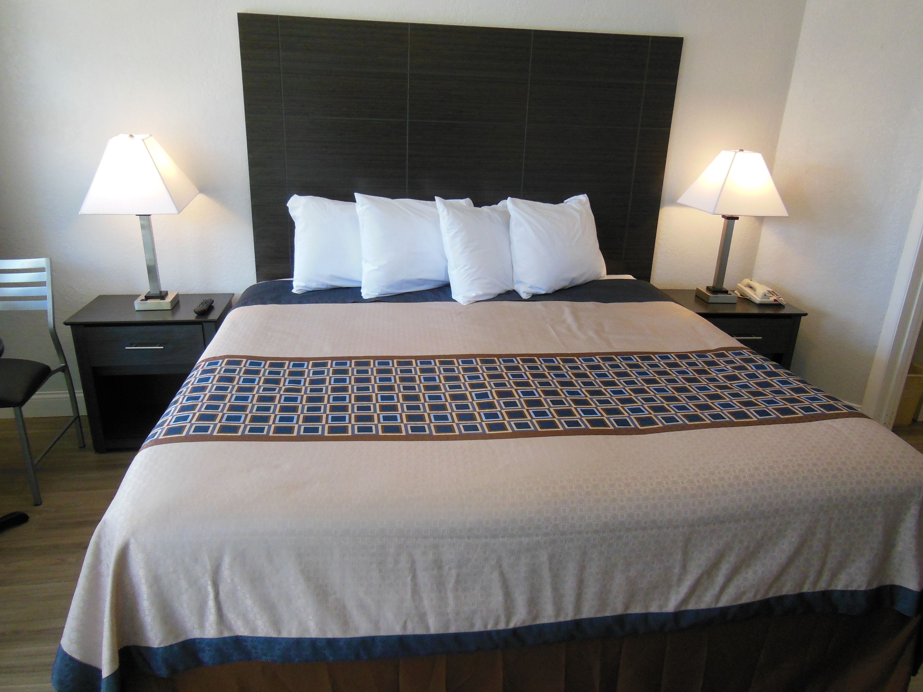 A neatly made bed with a patterned bedspread, two bedside lamps, a nightstand with a phone, and a chair.