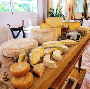 Variedad de quesos y frutos secos sobre una mesa de madera en una habitación con ventanas y sillas.