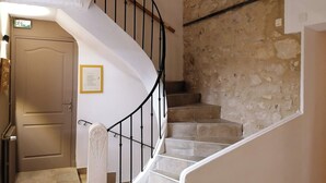 Una escalera en espiral con un muro de piedra, una puerta con un certificado enmarcado y un radiador.