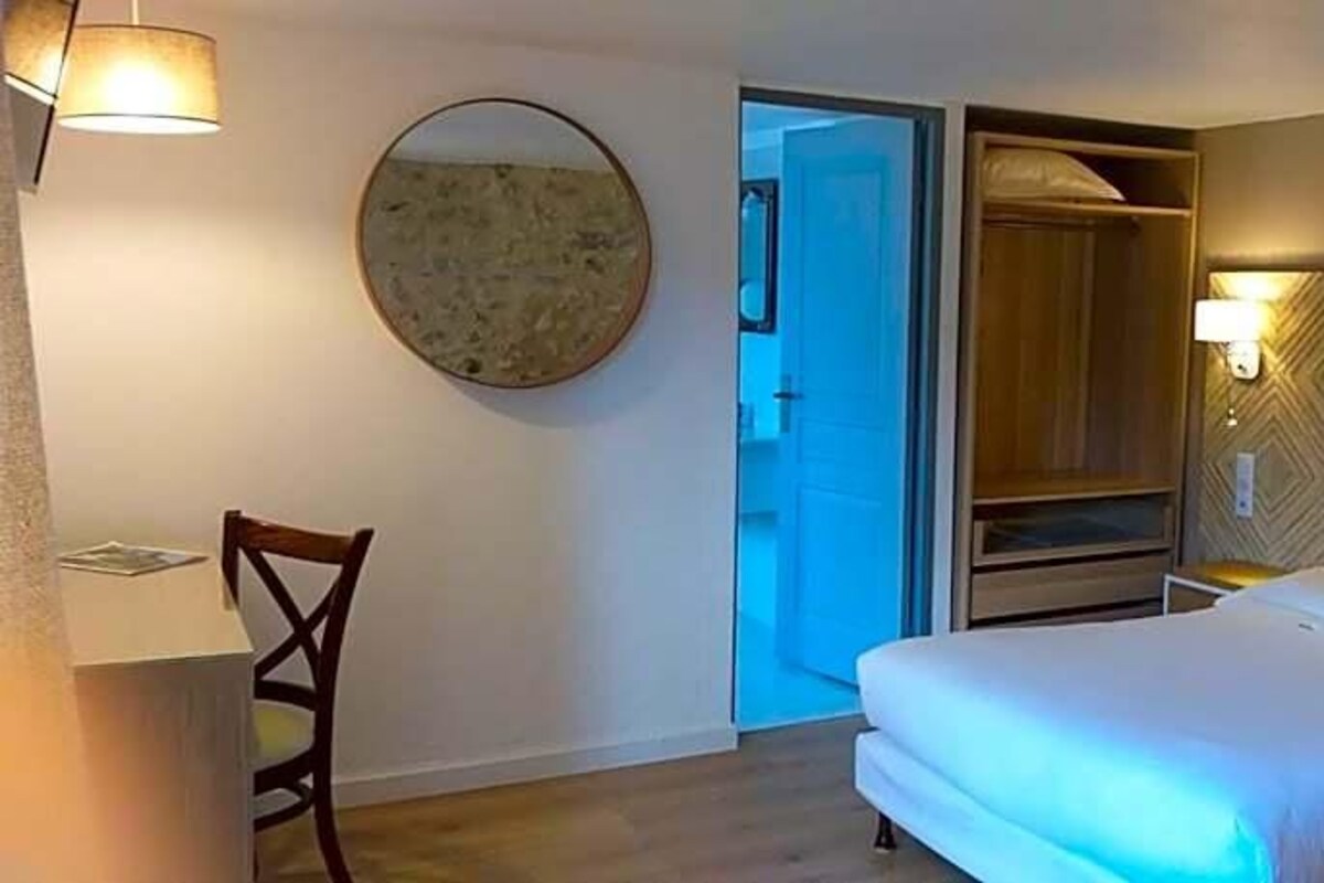 Una habitación de hotel con cama, una silla, escritorio, espejo y armario.