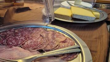 Un bufé con carnes y quesos en porción, cubiertos por una cúpula de vidrio.