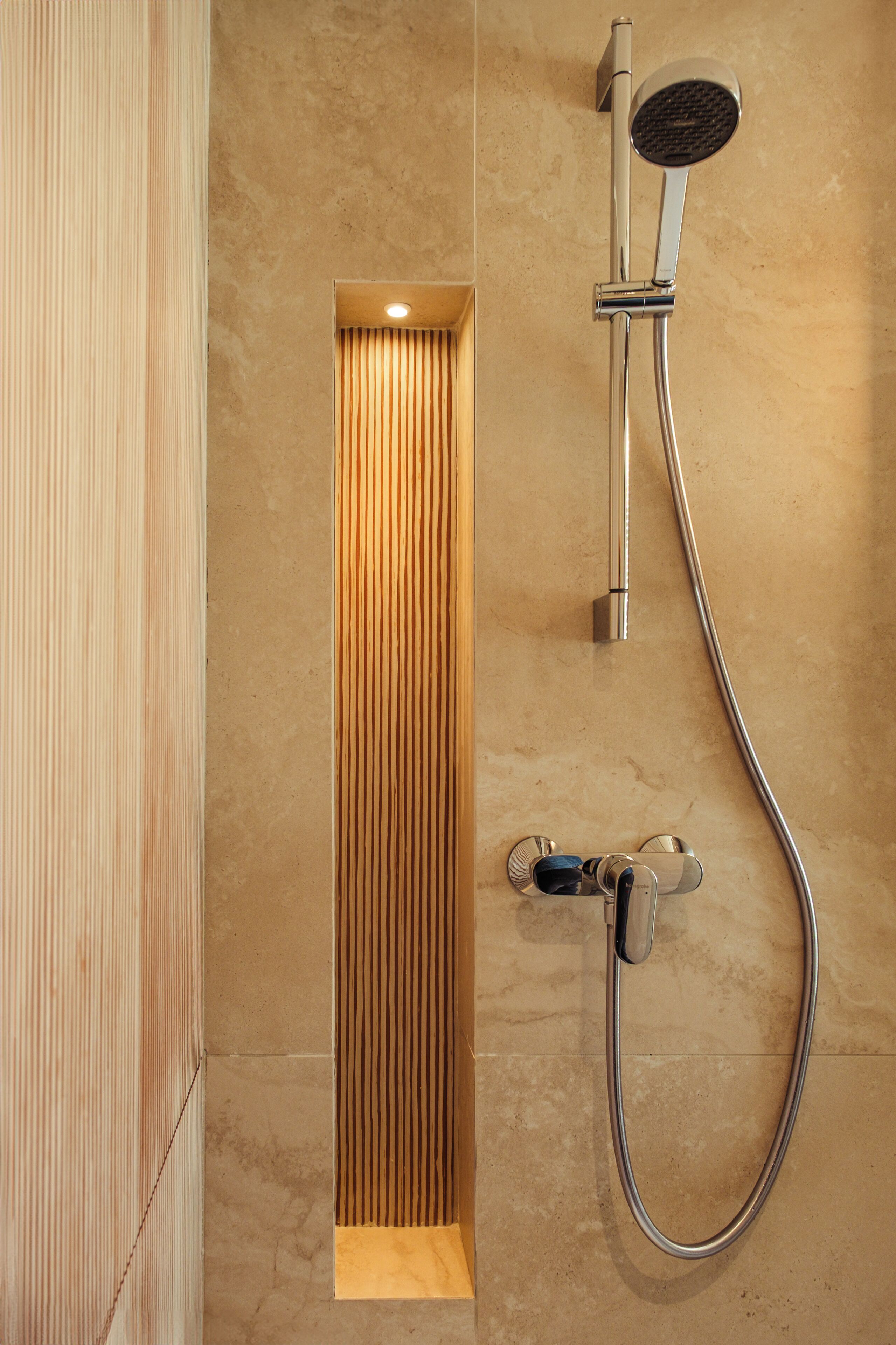 A modern shower with a vertical panel, a handheld showerhead, and a wall-mounted control.
