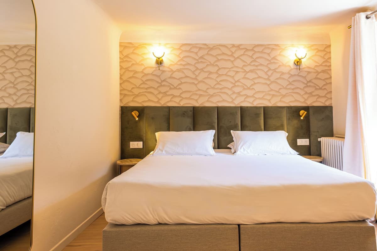 Ein Hotelzimmer mit einem großen Bett, zwei Wandleuchten, einer Heizung und einem Spiegel.