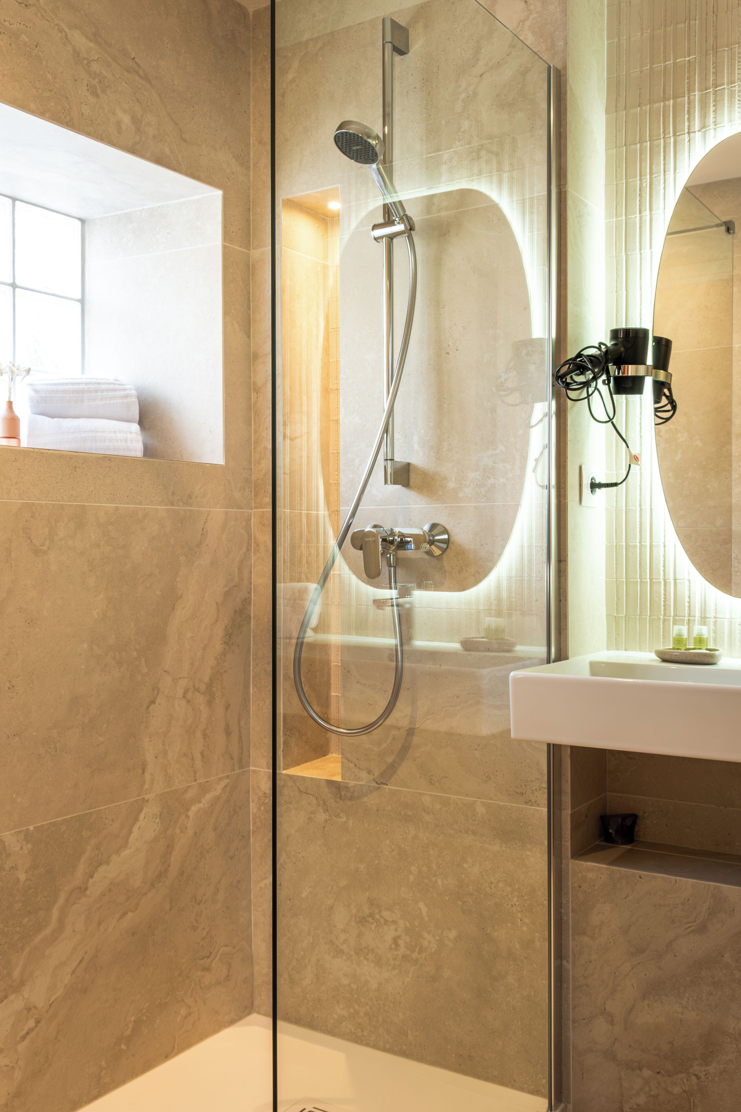 A modern bathroom with a glass-enclosed shower, a white sink, and a large mirror.