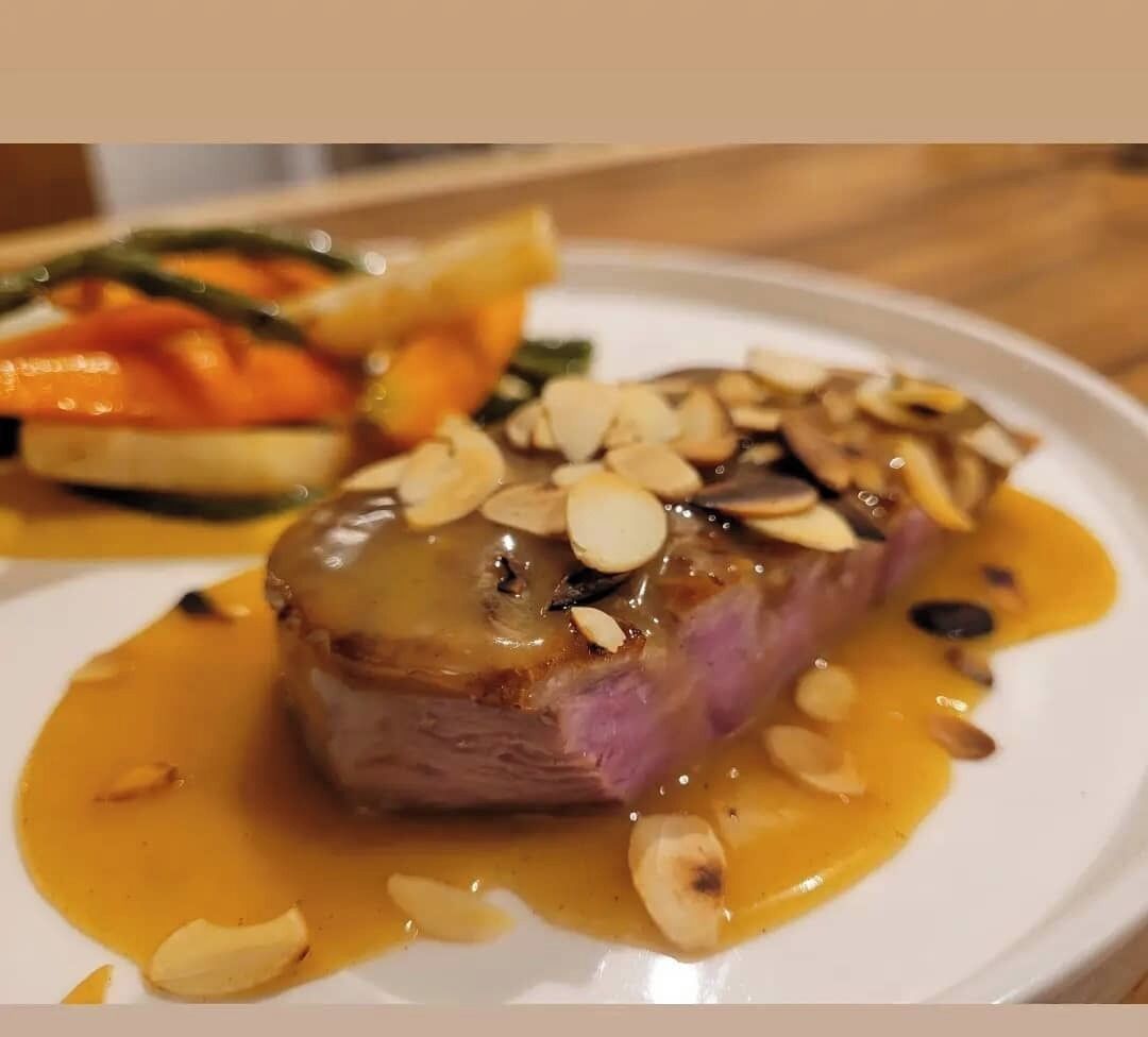 Un plato de comida con un trozo de carne cubierto de almendras y salsa.