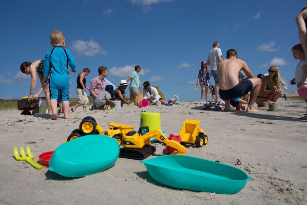 Una playa arenosa con gente, incluyendo niños jugando con vehículos y juguetes de arena.
