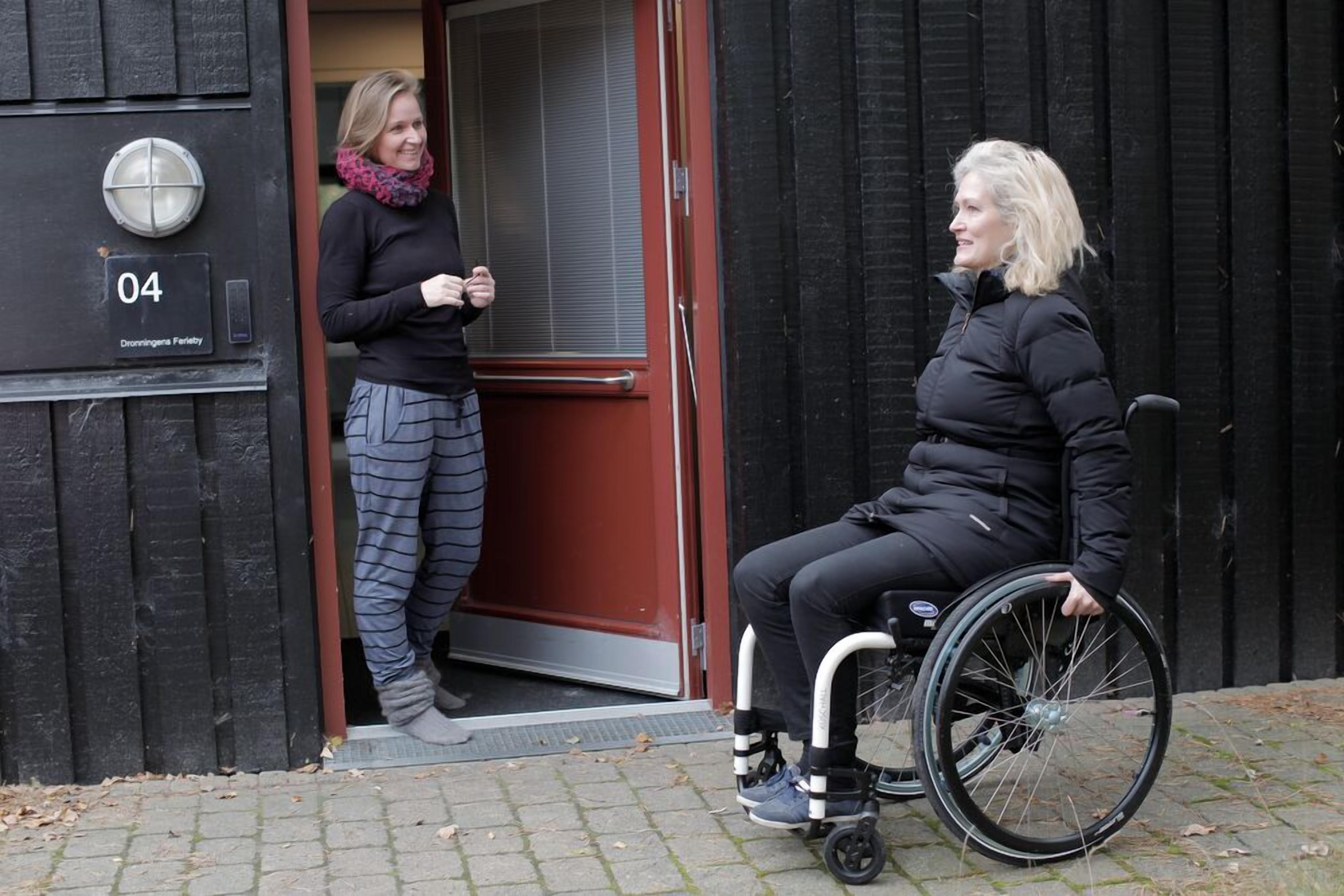A person in a wheelchair outside a building with a door marked '04' and a sign that reads 'Dronningenestraat Ferbey'.