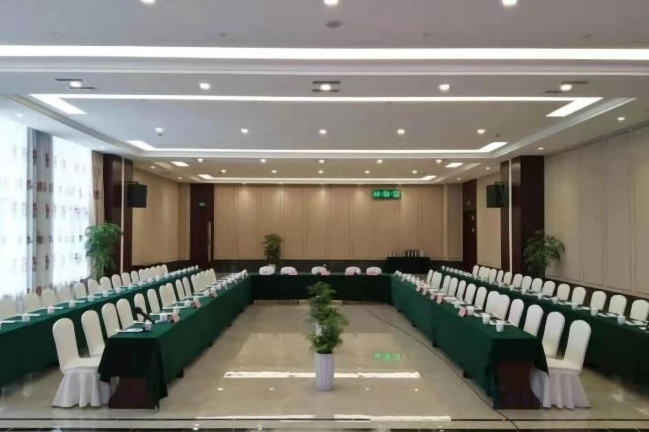 Un salón de conferencias con una mesa larga, sillas blancas y un mantel verde.