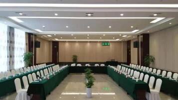 Un salón de conferencias con una mesa larga, sillas blancas y un mantel verde.
