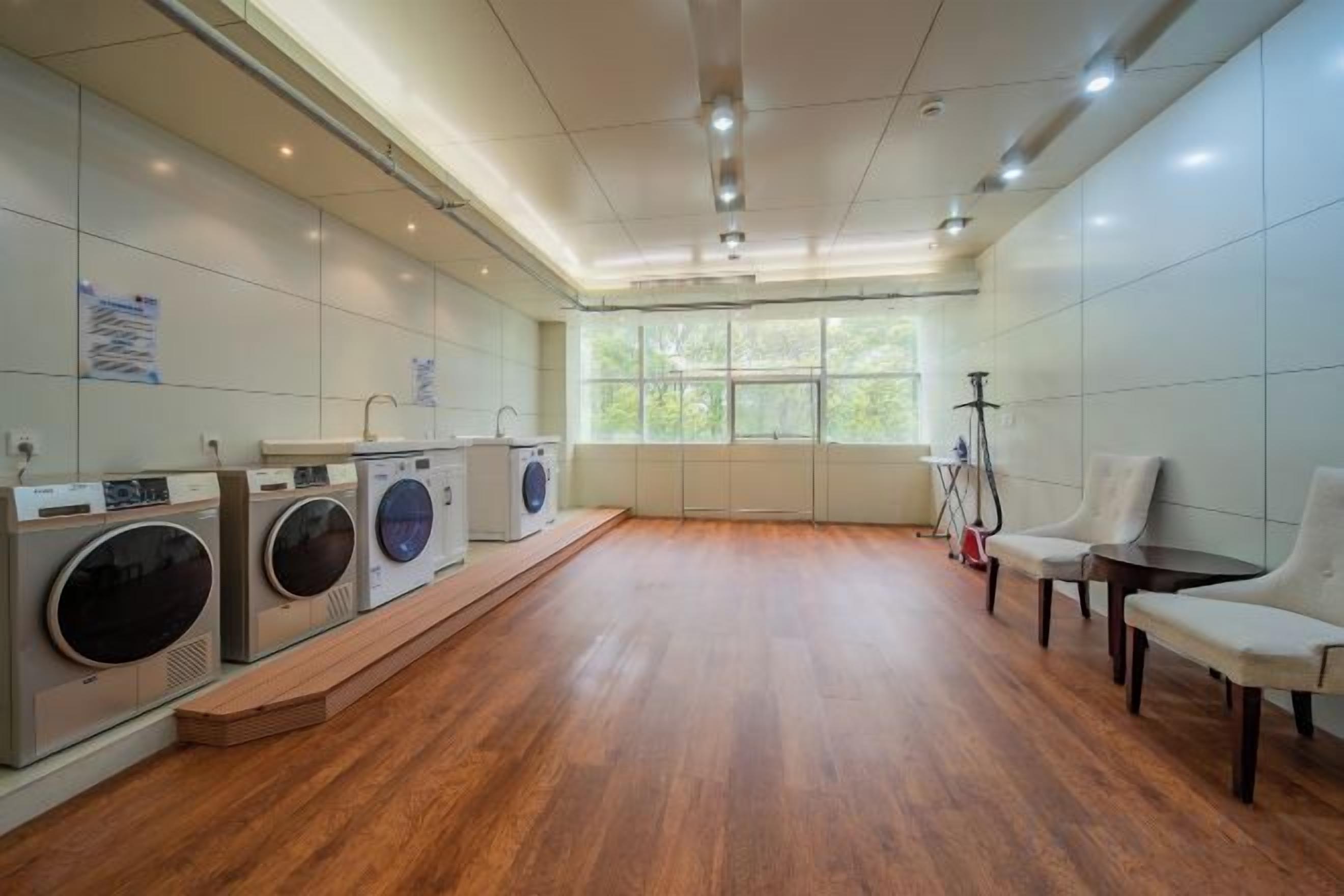 A laundry room with multiple washing machines, a wooden floor, and a window providing natural light.