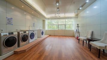 A laundry room with multiple washing machines, a wooden floor, and a window providing natural light.