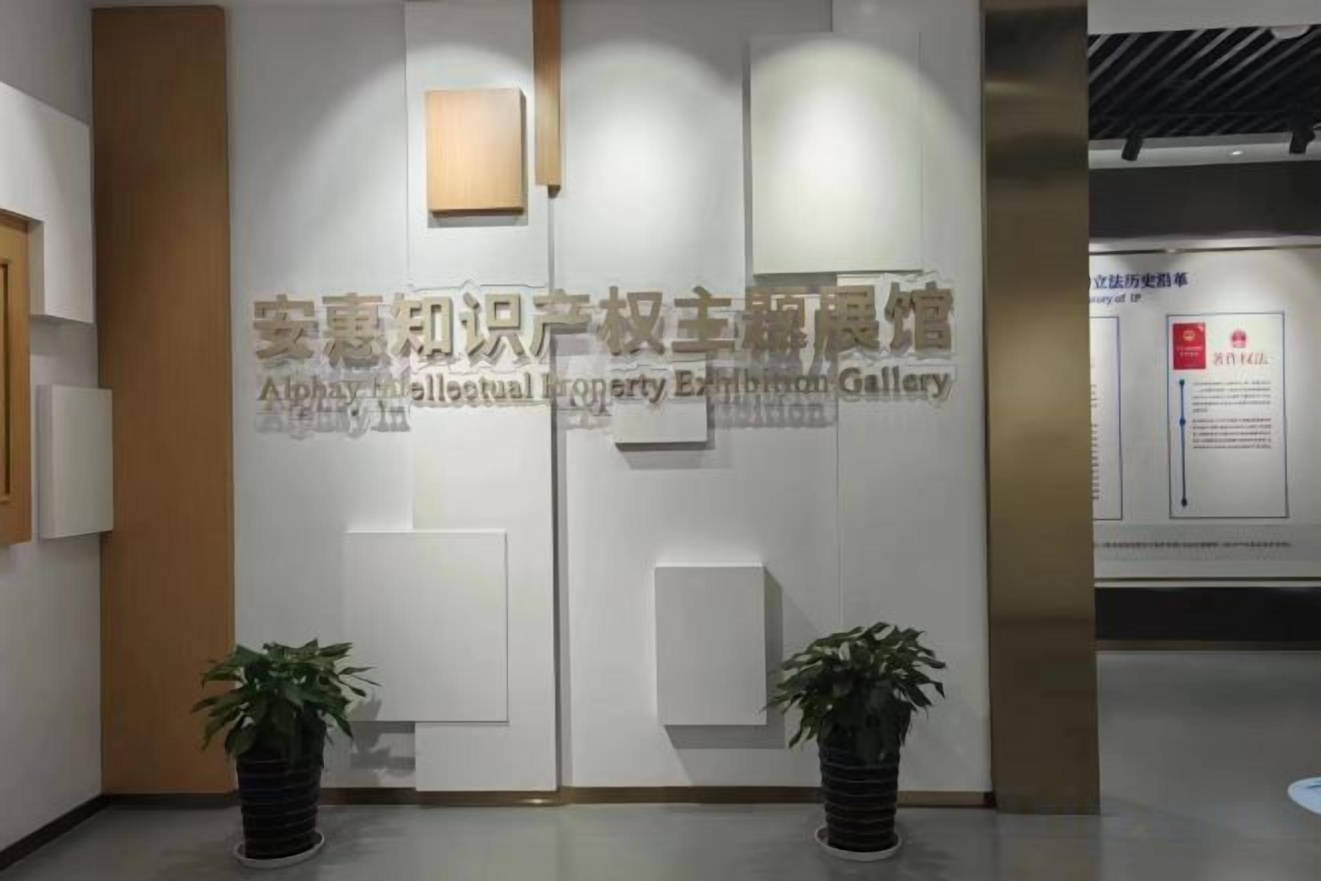A reception area with a modern design, featuring a wall-mounted sign with text, two potted plants, and a light fixture.