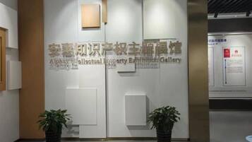 A reception area with a modern design, featuring a wall-mounted sign with text, two potted plants, and a light fixture.