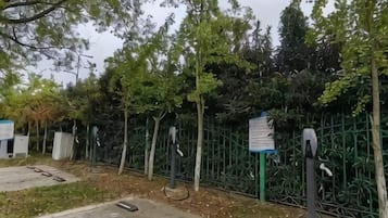 A parking area with electric vehicle charging stations, a fence, and a signboard.